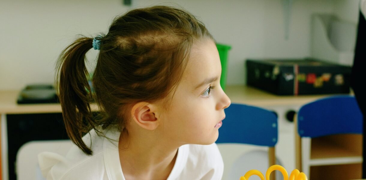 Niña sentada en un escritorio de salón de clases, mirando hacia un lado con atención