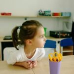 Niña sentada en un escritorio de salón de clases, mirando hacia un lado con atención