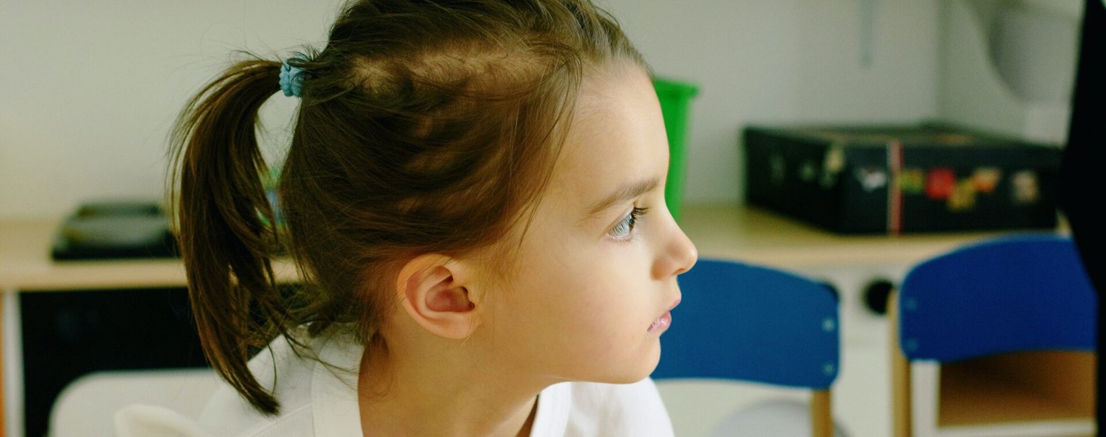 Niña sentada en un escritorio de salón de clases, mirando hacia un lado con atención